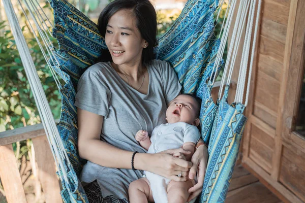 Mother holding daughter while resting on hammock — 图库照片