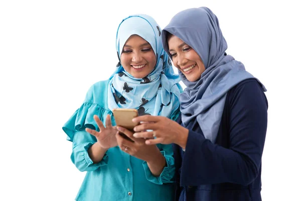 Portret van een gesluierde jonge vrouw die een smartphone aan haar moeder laat zien en het samen ziet — Stockfoto