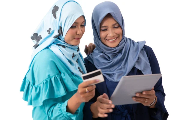 Portrait of young veiled woman holding a credit card and showing a tablet to her mother — Stock Photo, Image