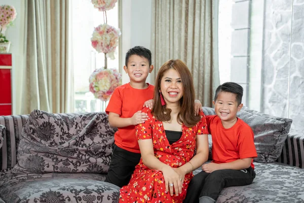 笑着坐在沙发上的中国母亲和两个穿着红色主题衣服的儿子 — 图库照片