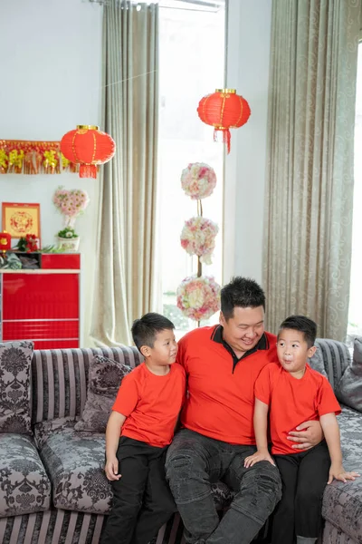 Smiling asian chinese father and two son wearing red theme clothing sitting on the sofa