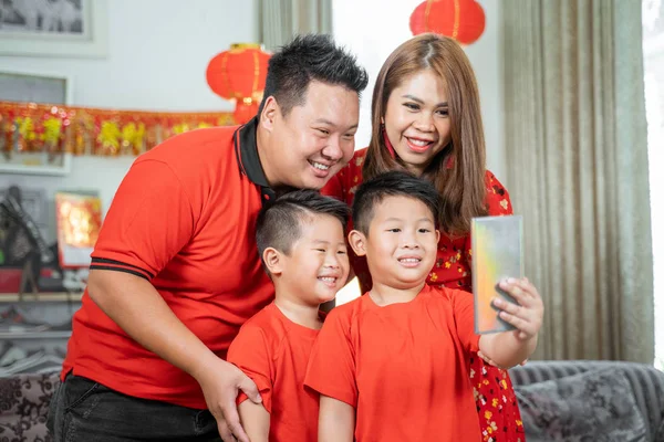 Asian family with two son smiling holding cell phone to take selfie with father and mother