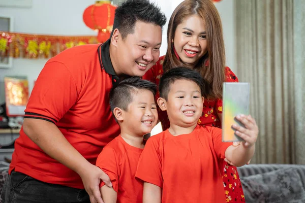 Asian chinese family with two son smiling holding cell phone to take selfie with father and mother