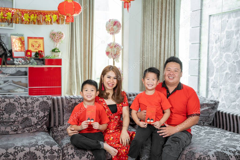 Asian chinese family with two son holding ang pao smiling when sitting on sofa