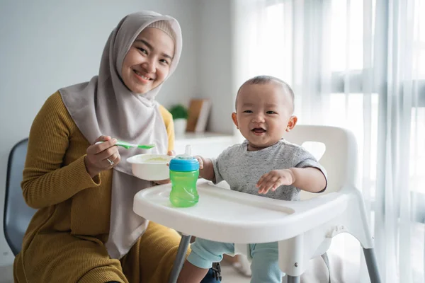 Mother feeding her baby boy while sitting on high chair — 스톡 사진