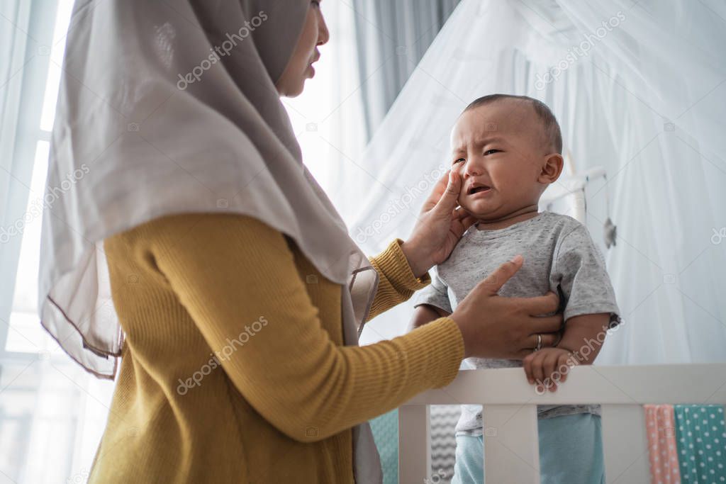 mother try to comfort her cry child at the crib