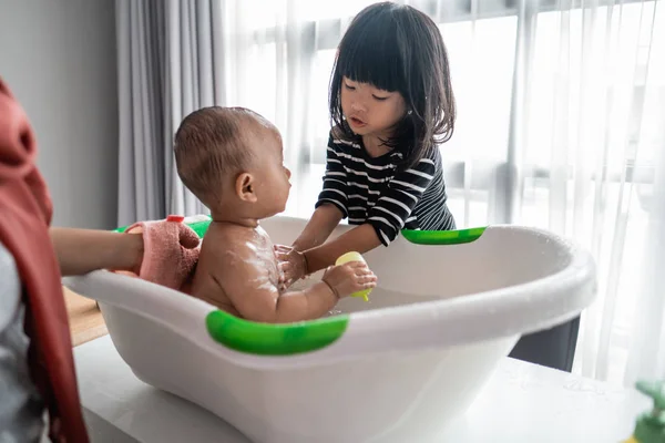 Hermana útil lavar a su hermano bebé durante la hora del baño —  Fotos de Stock