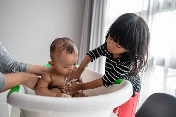 Hermana útil lavar a su hermano bebé durante la hora del baño — Foto de Stock