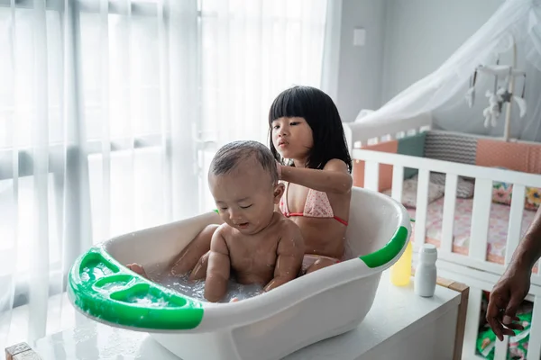 Menina tomando banho de seu irmãozinho em uma bacia — Fotografia de Stock