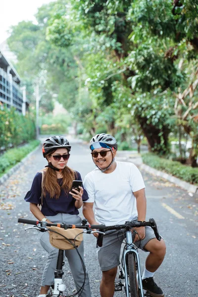 Pareja asiática que llevaba cascos con teléfonos celulares parecía feliz de andar en bicicleta juntos —  Fotos de Stock