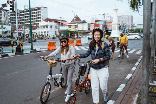 ヘルメットとバッグを身に着けている二人のアジアの若い女性は折りたたみ自転車で歩く — ストック写真