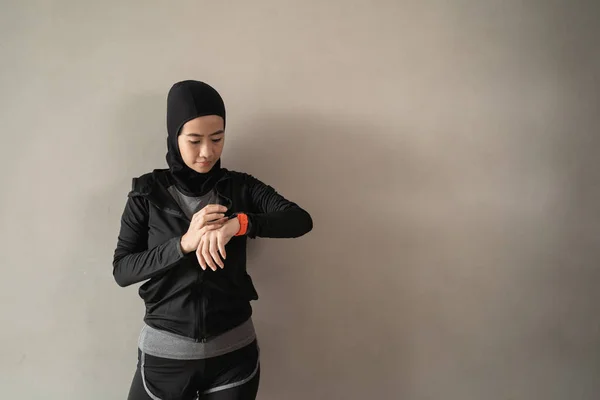 Hijab sporty mujer asiática mirando una pulsera inteligente para establecer la hora —  Fotos de Stock