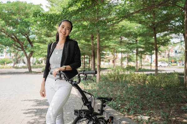 Sonriente mujer asiática joven trabajador de pie con su bicicleta plegable —  Fotos de Stock