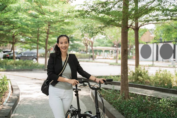 Sonriente mujer trabajadora camina en su bicicleta plegable a través del parque —  Fotos de Stock