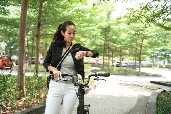 Mujer asiática mirando su reloj cuando camina con bicicleta plegable — Foto de Stock