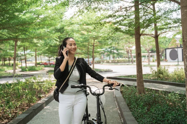 Sonriente mujer trabajadora camina con su bicicleta plegable mientras recibe una llamada telefónica — Foto de Stock