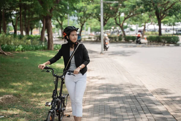 Asiático jovem mulher vestindo capacete depois de trabalho andando com sua bicicleta — Fotografia de Stock