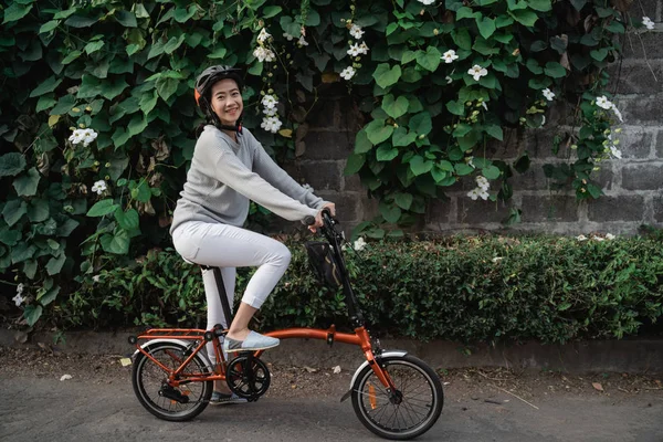 Mujeres jóvenes usan cascos para montar bicicletas plegables en el fondo ornamental de la planta —  Fotos de Stock