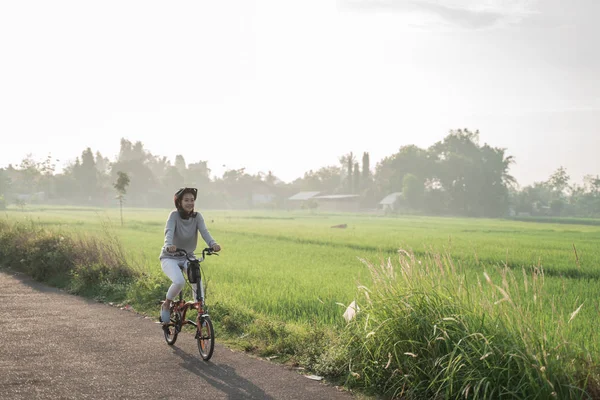 Jonge vrouwen dragen helmen om fietsen te rijden in rijstvelden achtergrond — Stockfoto