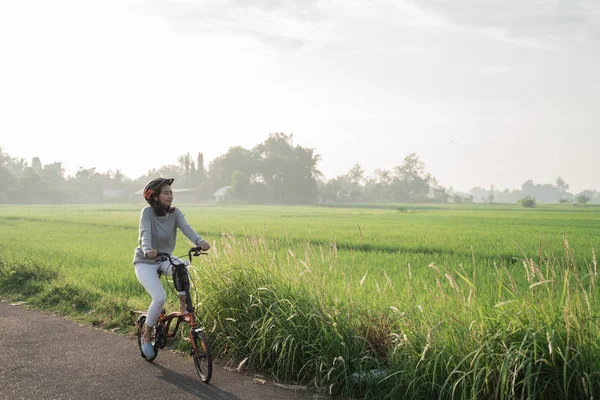 Asian women wear helmets to ride folding bikes in the rice fields — Stock Photo, Image