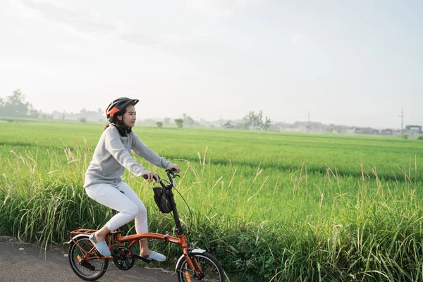 Mujeres jóvenes usan cascos para montar bicicletas plegables en el fondo de campos de arroz — Foto de Stock