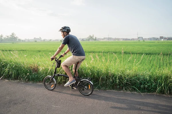 Junge asiatische Männer tragen Helme, um auf den Reisfeldern Klappräder zu fahren — Stockfoto