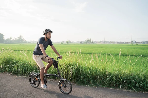 Junge asiatische Männer tragen Helme, um auf den Reisfeldern Klappräder zu fahren — Stockfoto