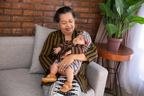 Asiatische lächelnde Großmutter mit schlafendem kleinen Enkel in javanischem Batik — Stockfoto