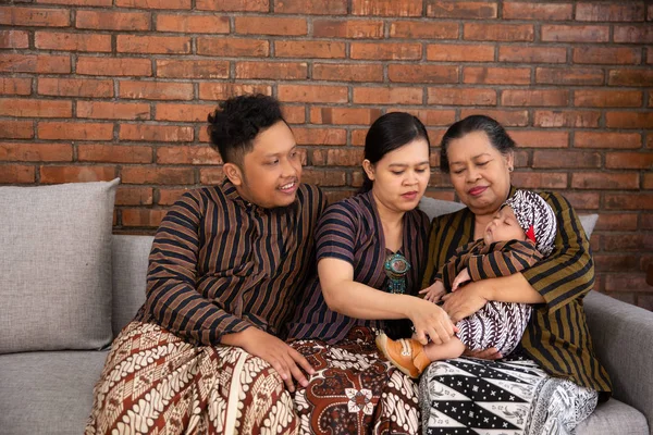 Divertirse de asiático feliz familia sentado en sofá usando javanese batik patrimonio —  Fotos de Stock