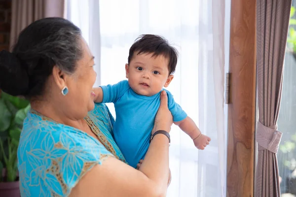 Lächelnde asiatische alte Frau steht mit tragendem kleinen Sohn — Stockfoto