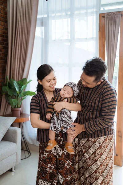 Padre y madre vistiendo batik javanés mirando soñoliento lindo pequeño hijo —  Fotos de Stock