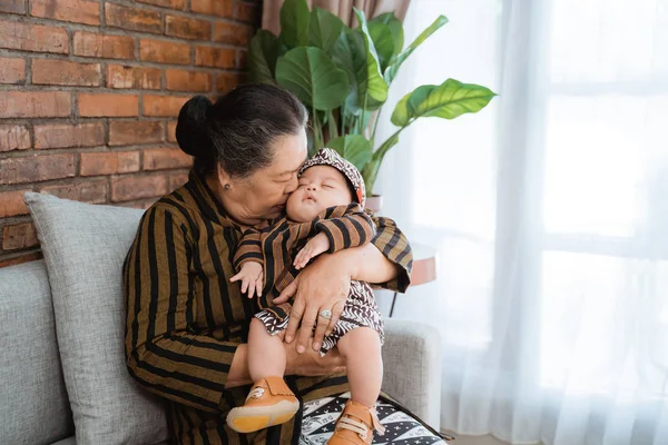 grandmother kissing sleeping little grandson when sits on sofa,wearing javanese batik