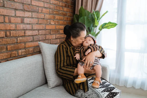 Nenek asia mencium cucu kecil yang sedang tidur mengenakan batik javanese — Stok Foto