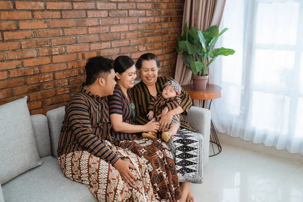 Tendo diversão de asiático feliz família sentado no sofá vestindo javanês batik património — Fotografia de Stock