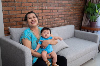 Gülümseyen büyükanne kucağında torunuyla oturuyor.