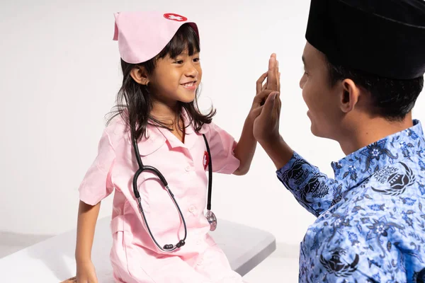 Ayah asia mengenakan batik korpri dengan lima tangan tinggi oleh putrinya mengenakan seragam dokter — Stok Foto