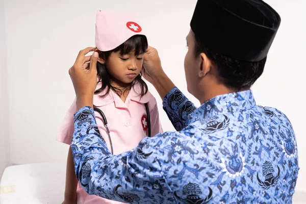 Asian father wearing batik korpri dress his daughter in a doctors uniform — Stock Photo, Image