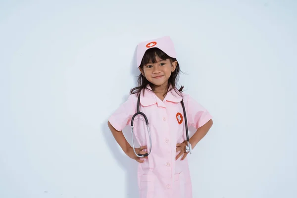 Söt asiatisk liten flicka bär läkare uniform med händerna på midjan — Stockfoto
