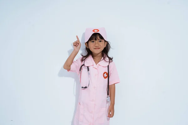 Söt asiatisk liten flicka bär läkare uniform med pekfingret uppåt — Stockfoto
