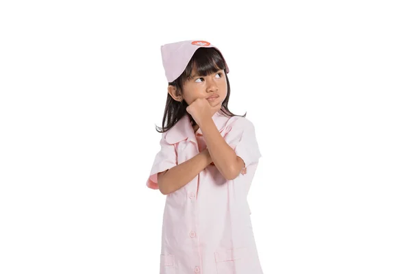 Asian little girl wearing a nurse uniform with one hand holding her chin — Stock Photo, Image