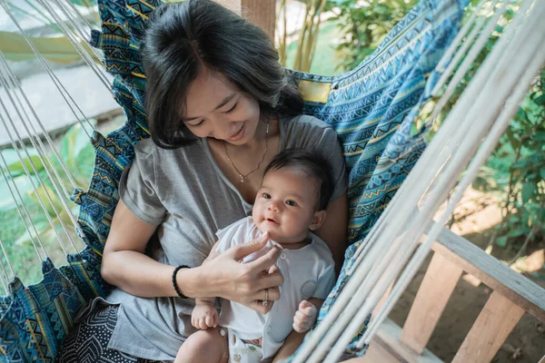 Mother holding daughter while resting on hammock — 图库照片