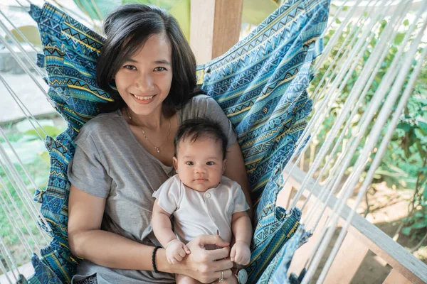Asian mother holding baby while resting on hammock — 图库照片