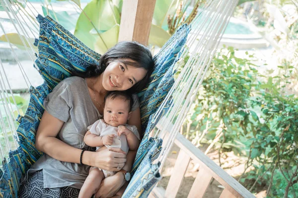 Mãe segurando filha enquanto descansa na rede — Fotografia de Stock