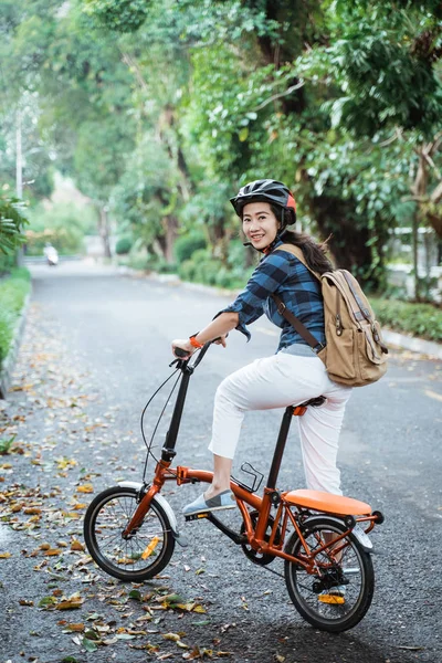 Glimlachende aziatische jonge vrouw dragen helm en tas rijden zijn vouwfiets — Stockfoto