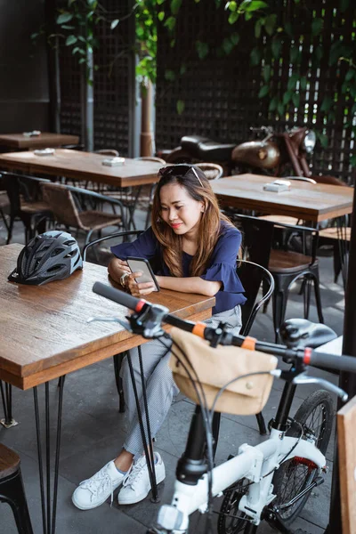 Mujer joven relajarse con el teléfono inteligente y descansar en la cafetería después de montar en bicicleta — Foto de Stock