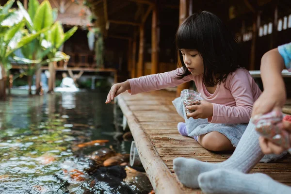 Två små flickor som har roligt utfodring koi fisk — Stockfoto