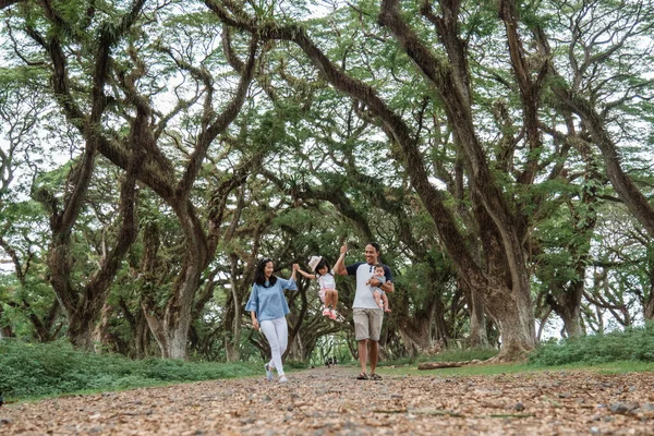 Ibu dan ayah dan dua anak tersenyum berjalan melalui pohon besar — Stok Foto