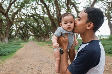 Asyalı baba kucağında bebekle öpüşüyor.