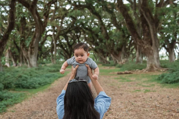 Asiático madre sosteniendo hasta un bebé en el parque — Foto de Stock