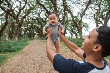 Asyalı baba kucağında bir bebekle güler.